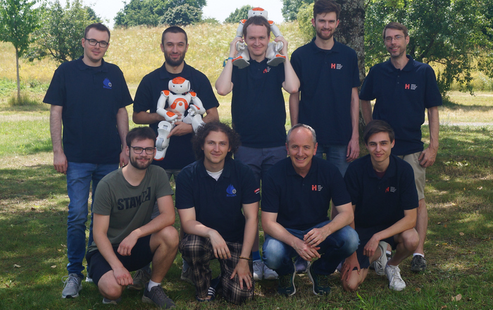 Teamfoto mit Robotern unter einem Baum auf einer Wiese