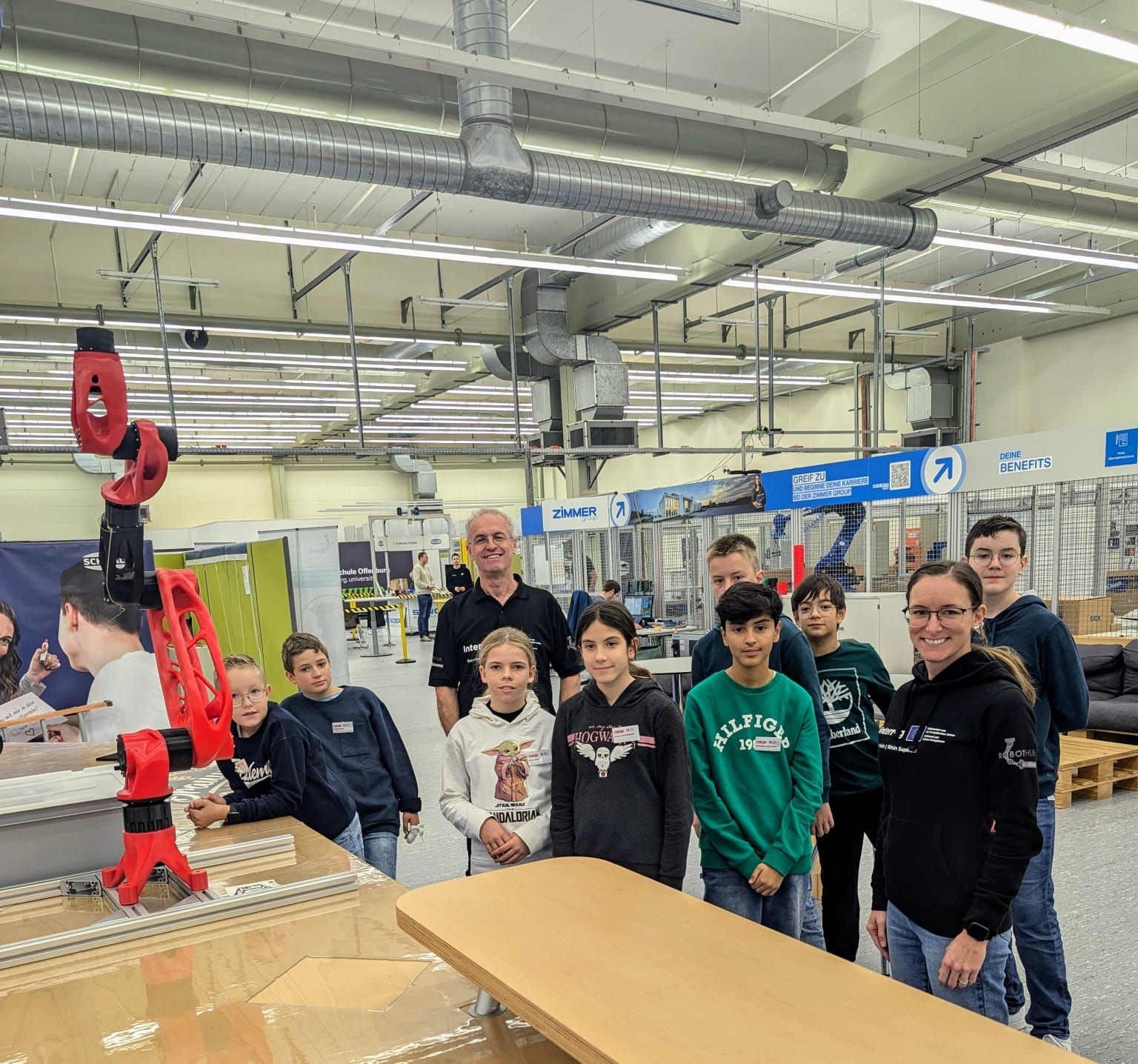 A man and a woman with a group of children stand next to a table with a robotic arm