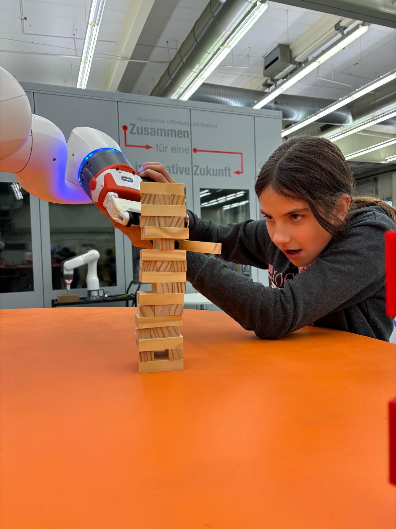 A girl manipulates a robot arm to play Jenga (with wooden blocks)