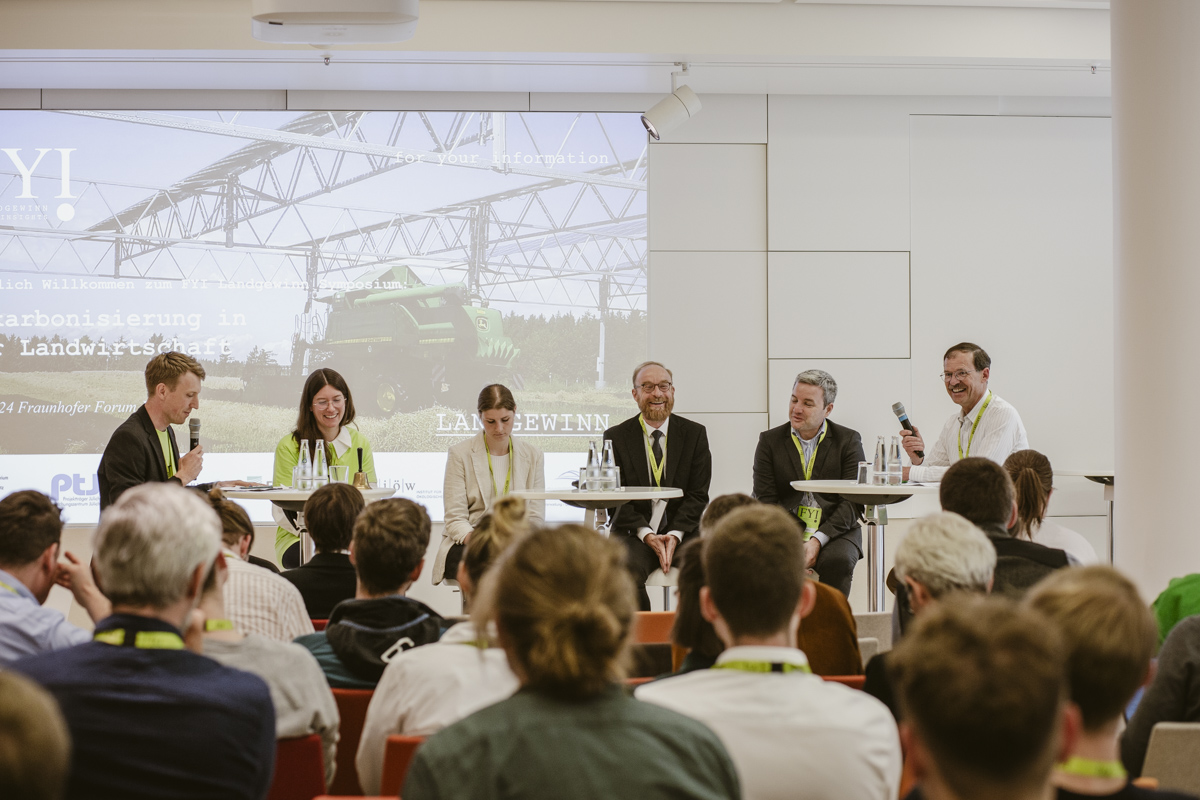 Die Beteiligten der Podiumsdiskussion sitzen nebeneinander auf der bühne vor den sitzenden Zuhörenden