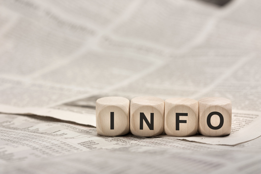 vier Würfel mit den Buchstaben INFO liegen auf einer Zeitung.
