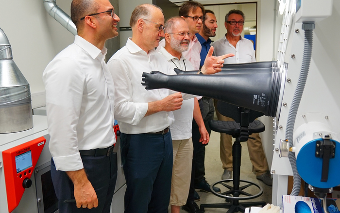 Eine Reihe von Männer steht vor den Gloveboxen aus denen "Plastikunterarme und -hände" herausragen